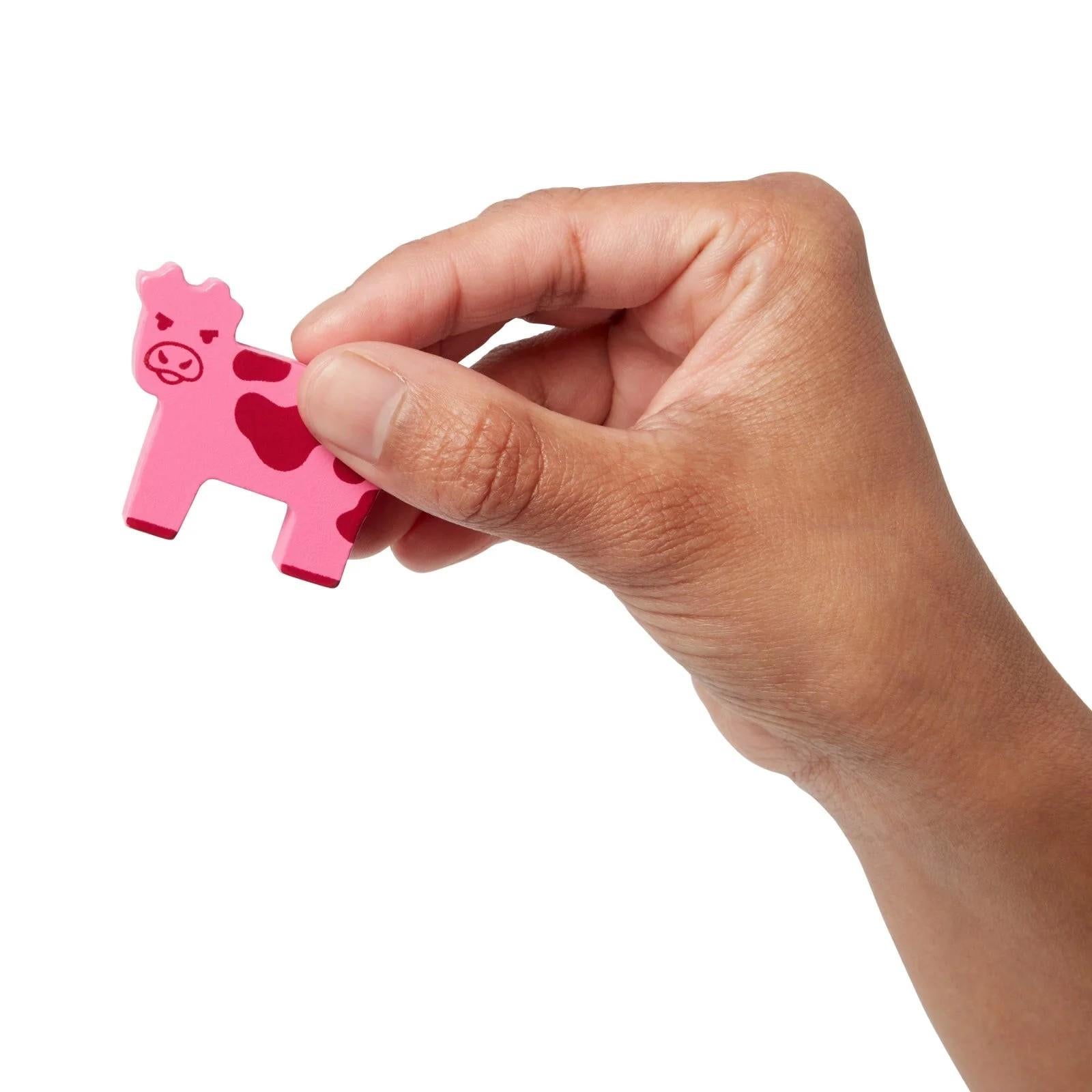 Hand holding a pink cow-shaped game token