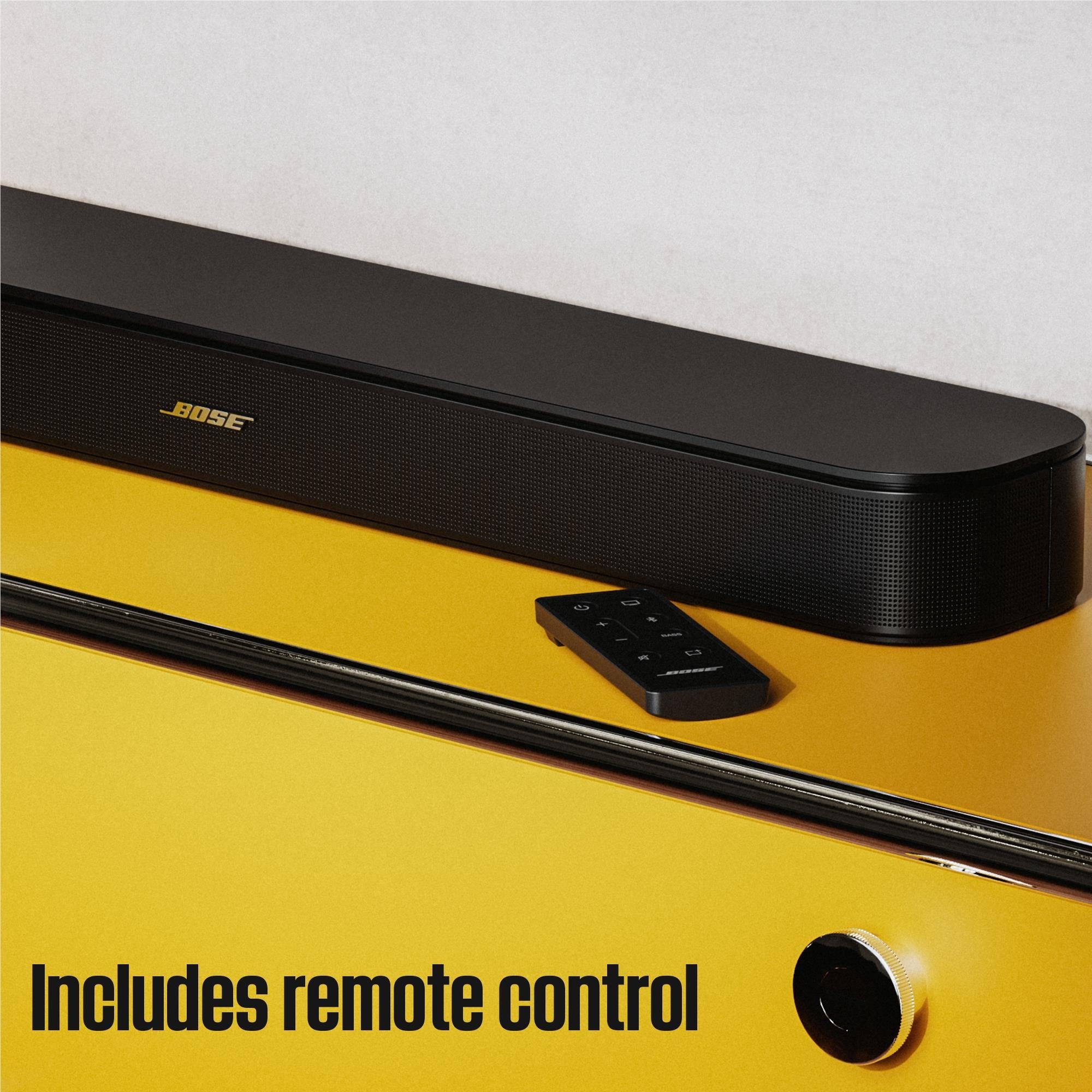Black Bose TV soundbar with included remote control beside the front panel.
