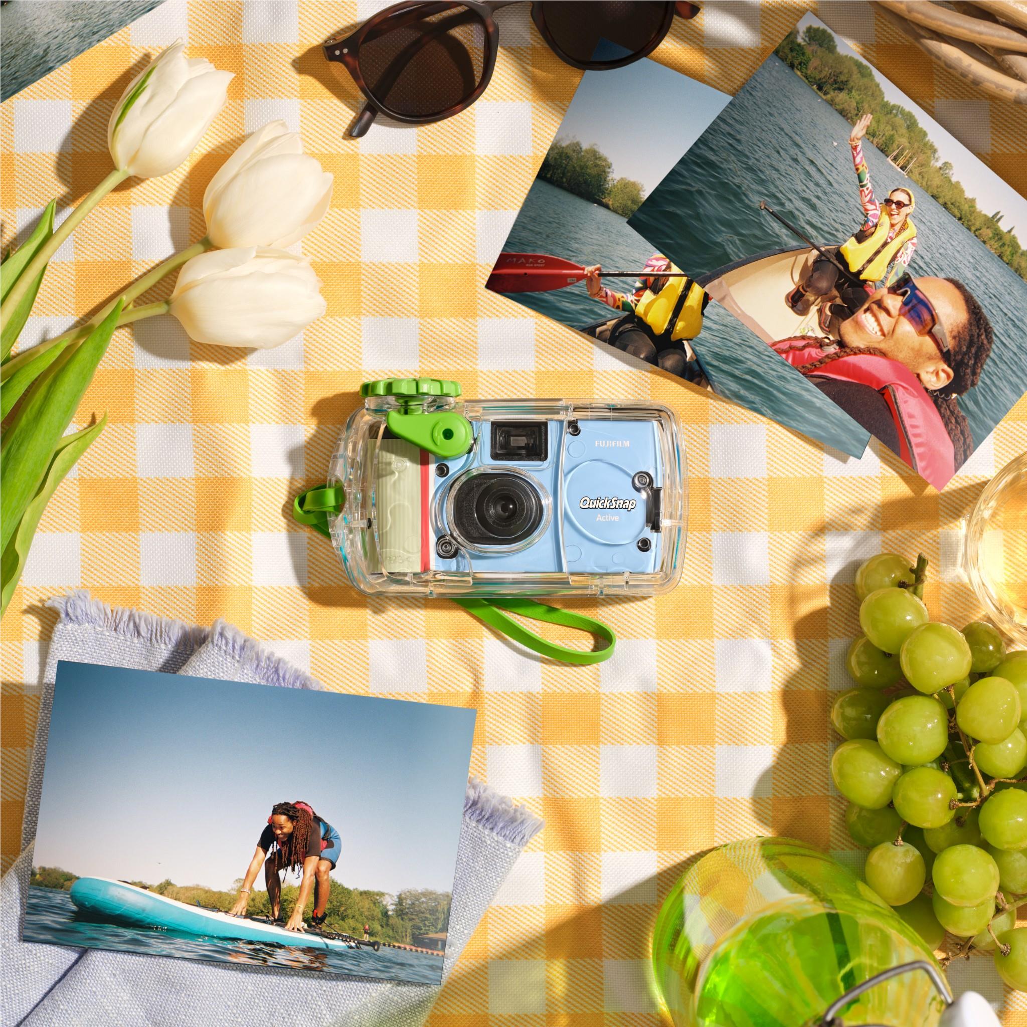 Clear disposable camera with green details on a plaid blanket with printed photos.