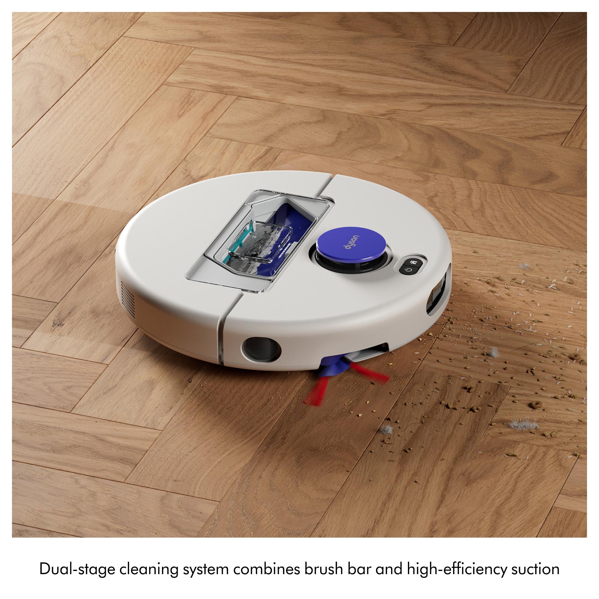 White robot vacuum with purple button on wooden floor, picking up debris