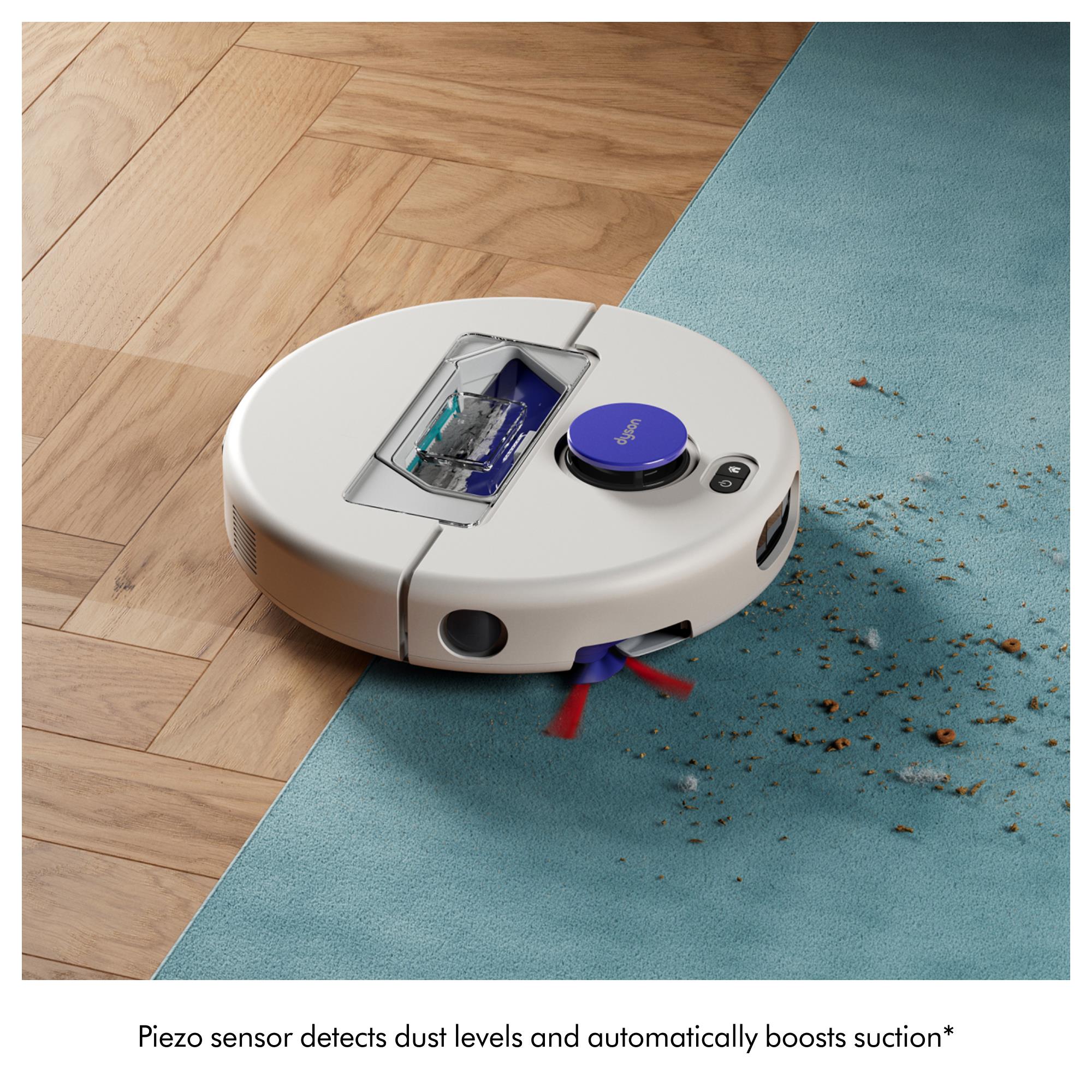 White robot vacuum on blue rug with purple top and debris near brush area