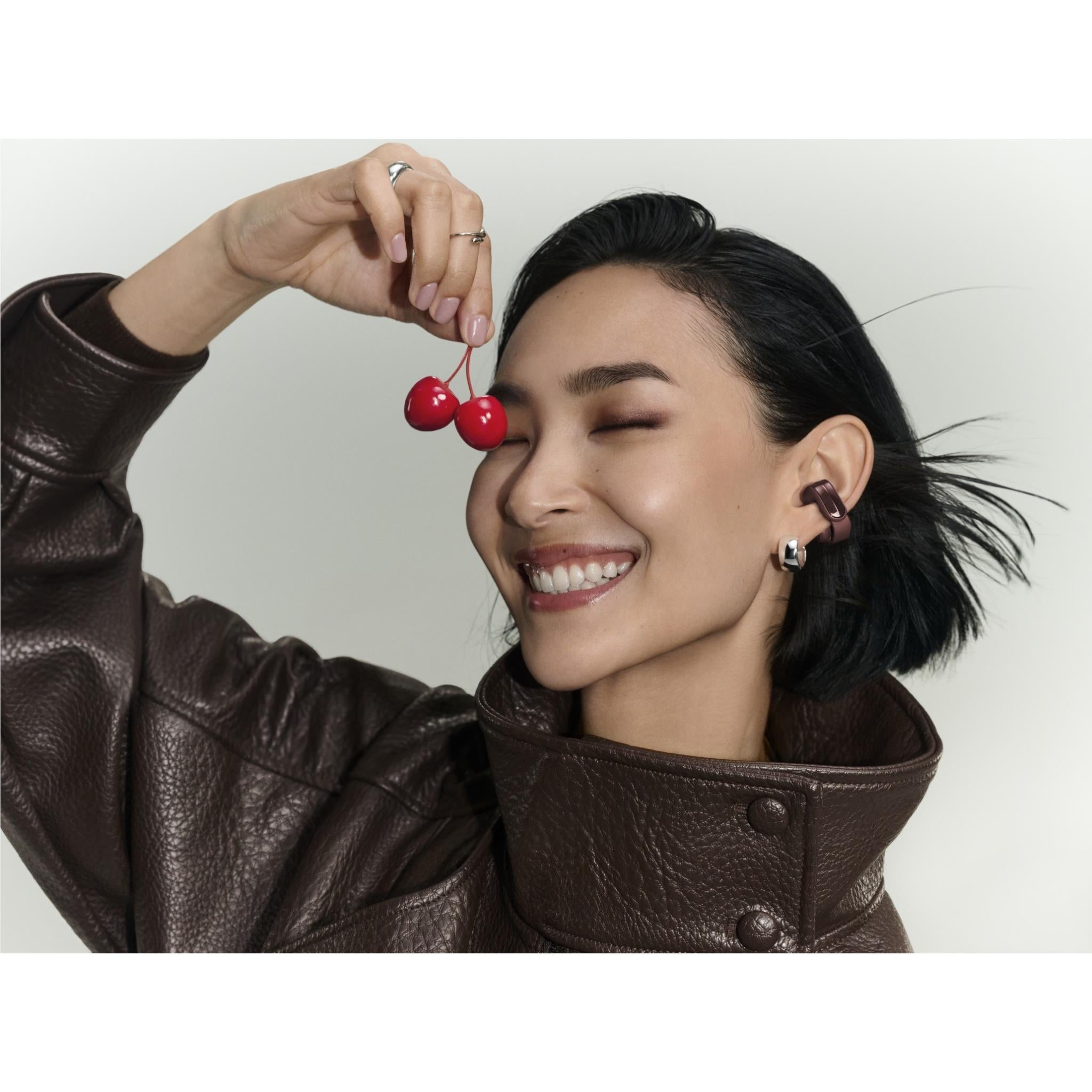 Open-ear earbuds on a woman’s ears in cherry chocolate, curved ear hooks visible