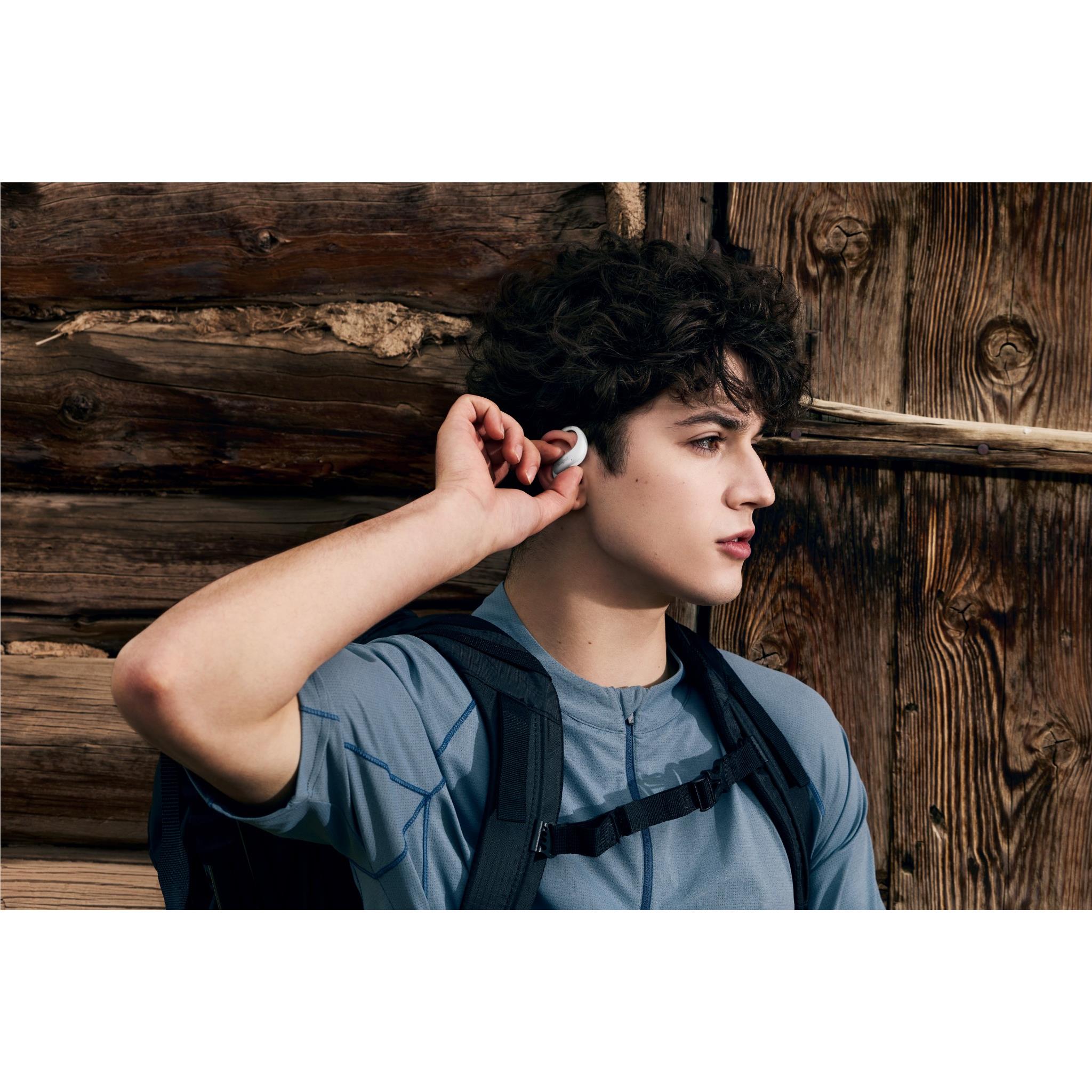 White open-ear wireless headphones on person’s ears, adjusting with fingers