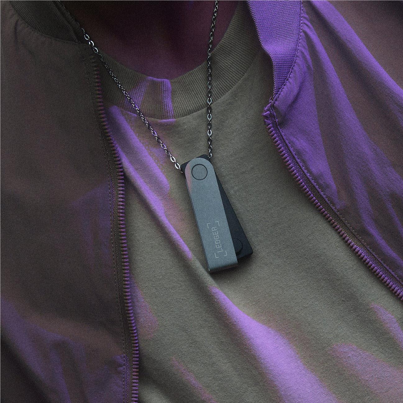 Ledger Nano X hardware wallet, pastel pink, hanging on chain against a jacket