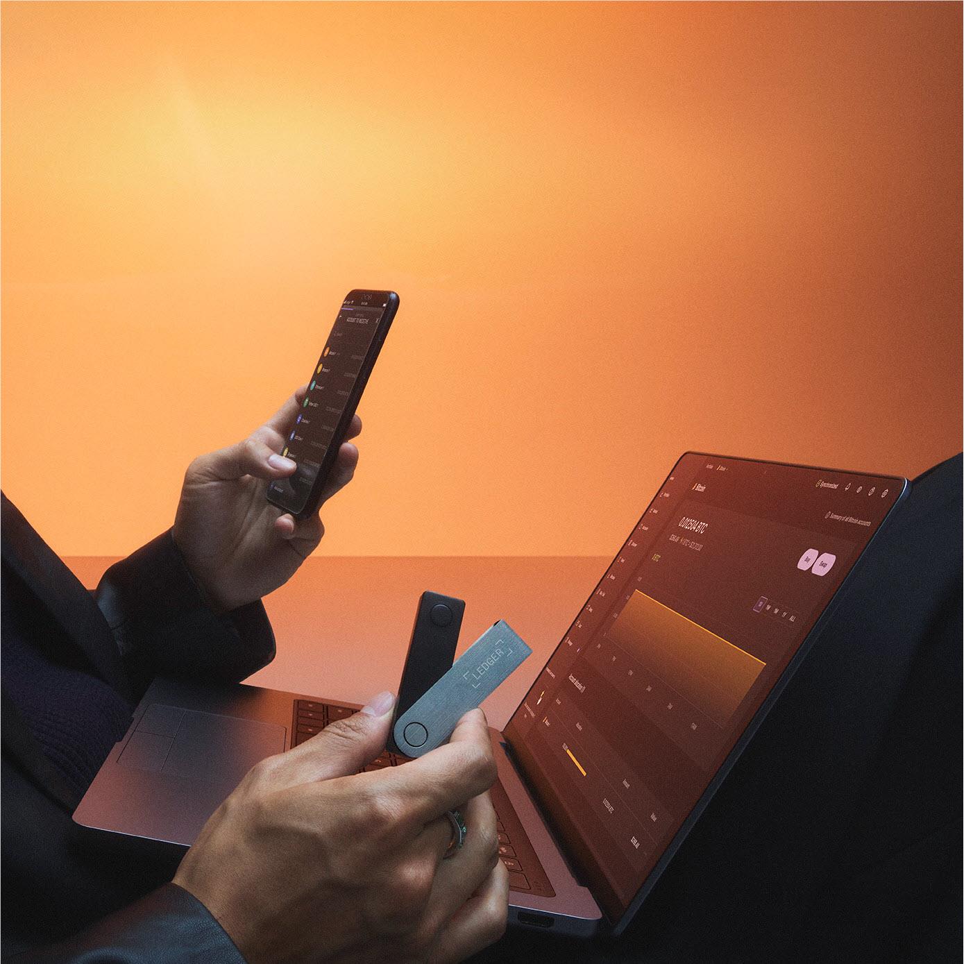 Hands using a Ledger crypto hardware wallet while checking a tablet app