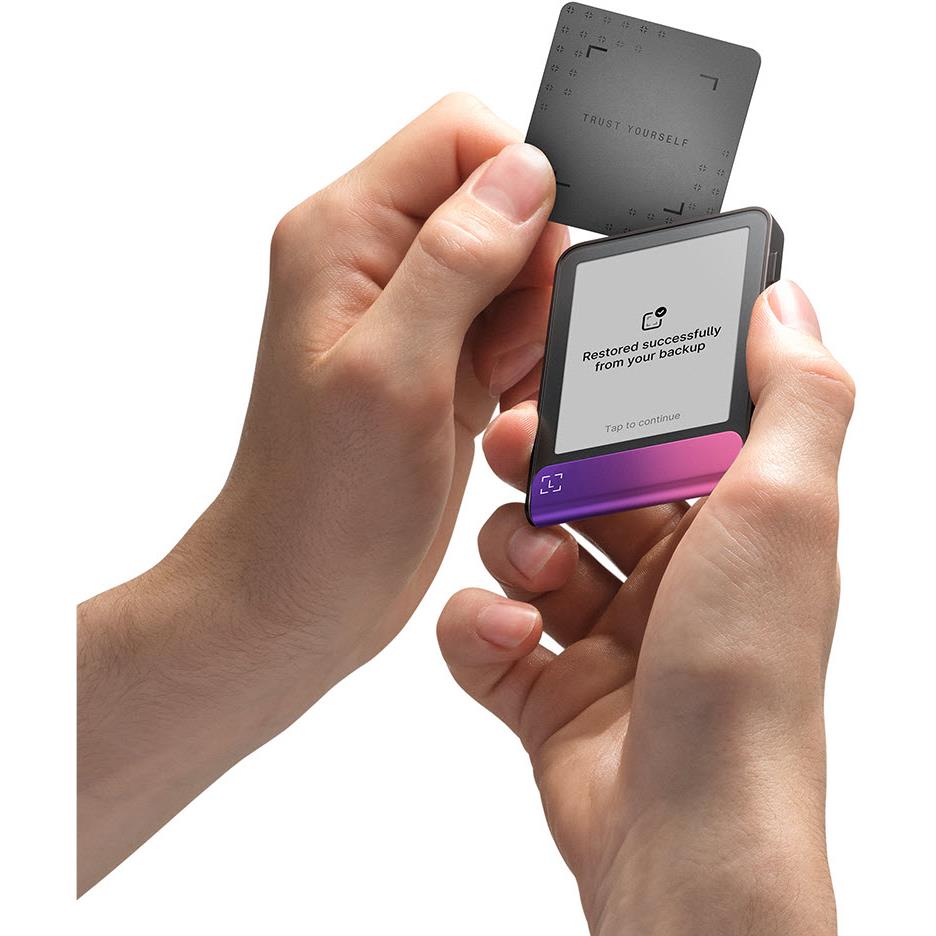Hardware wallet with status screen, held in hands; card behind, magenta base