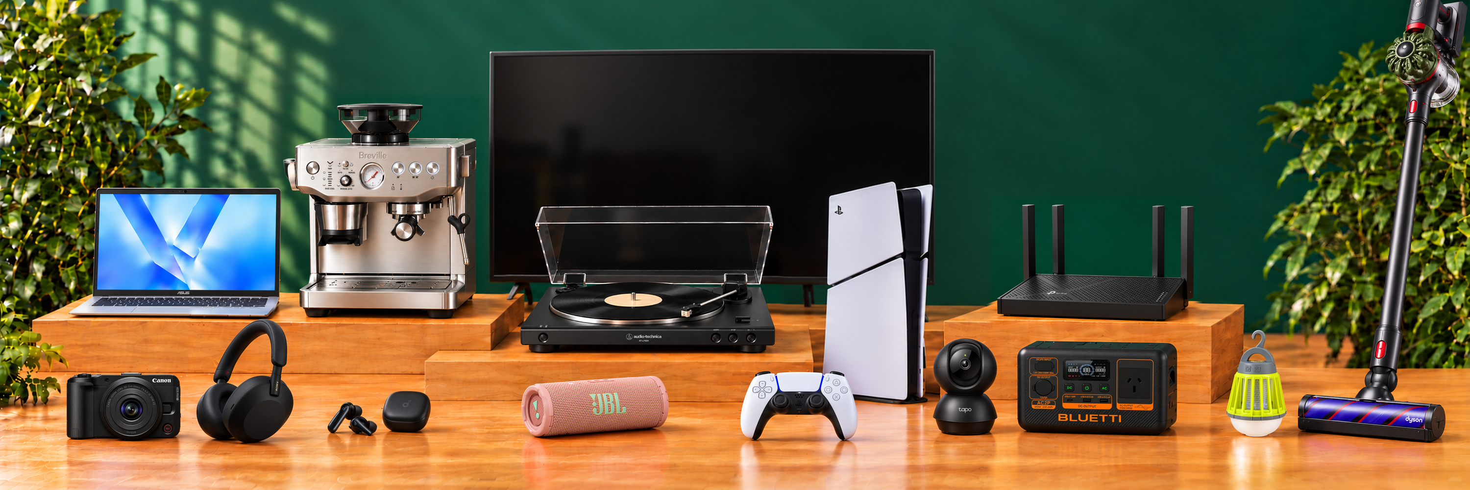 Tech Supply Shed product range displayed on wooden platforms, including a television, laptop, camera, headphones, turntable, PlayStation 5, coffee machine, networking equipment and cordless vacuum.