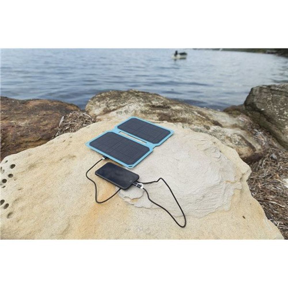 Foldable solar mobile charger on rocks with connected USB cable, outdoors